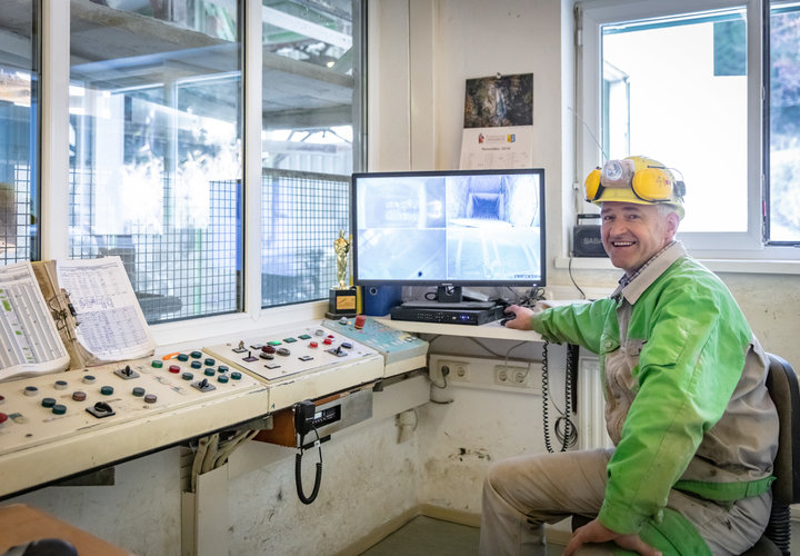 Ein Mitarbeiter steuert die Seilbahn im Bergbau und lacht in die Kamera. 